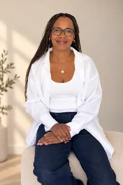 Simone Kirkpatrick, smiling, seated in a white linen shirt in a calm, light room